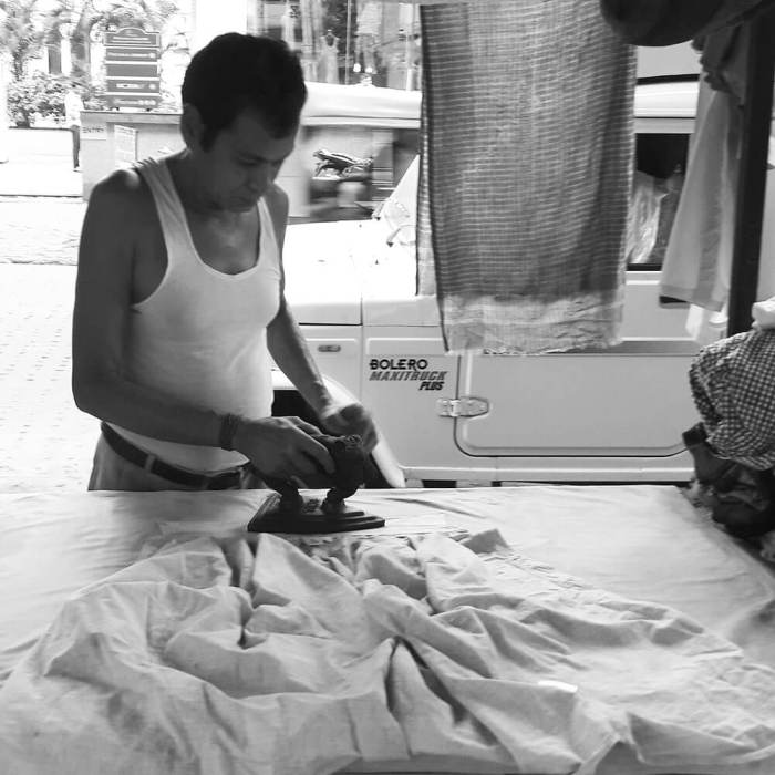 Man ironing shirt on street stall.