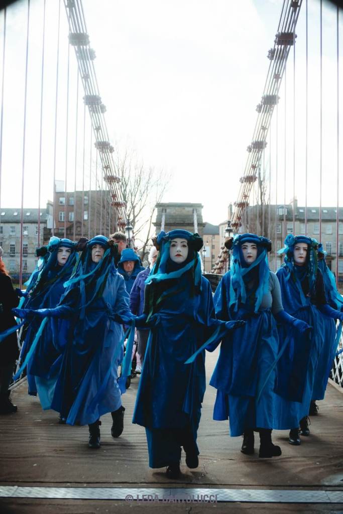 Blue figures walk down a pedestrian bridge