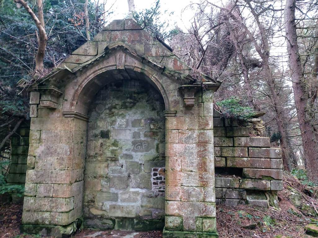 A crumbling mausoleum set amongst the woods. Trees are growing out of the roof of a mausoleum.